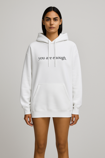 White hoodie with 'you are enough' text worn by a model on a gray background