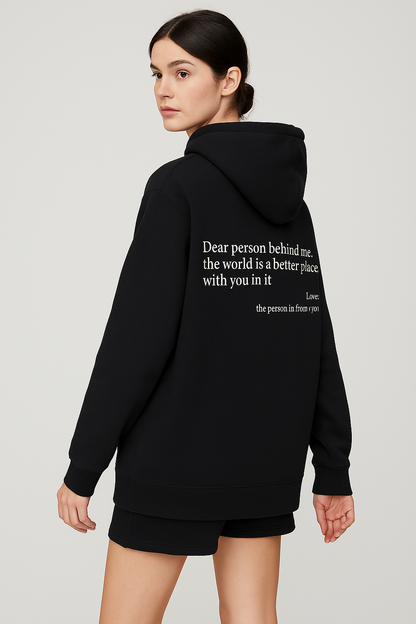 Person wearing a black hoodie with a quote on the back against a plain background