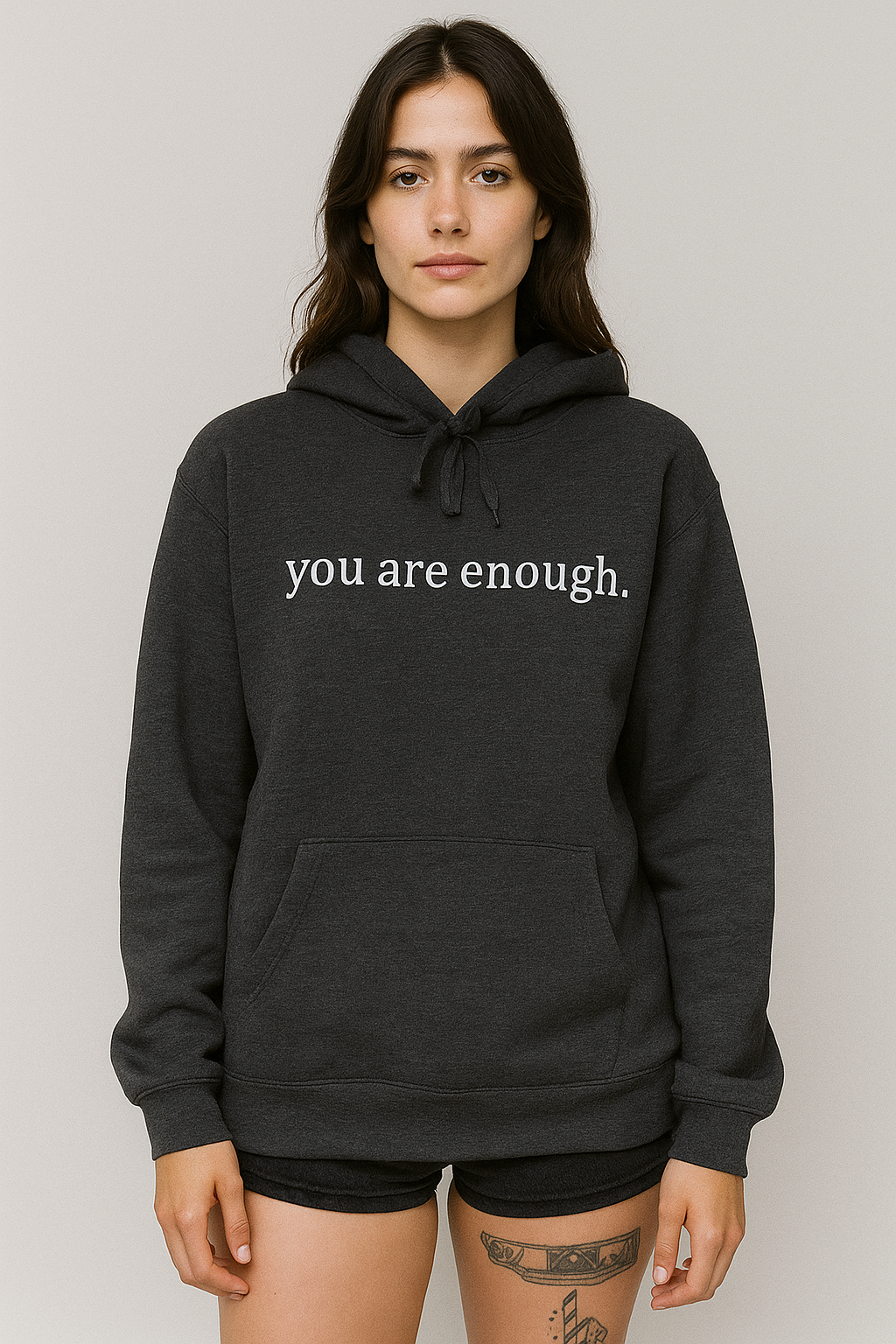 Person wearing a black hoodie with 'you are enough' text on a plain background