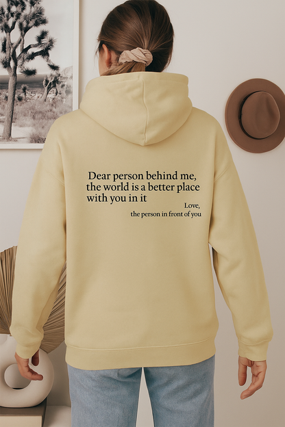 Person wearing a beige hoodie with a motivational quote on the back, standing in a room with decor elements.