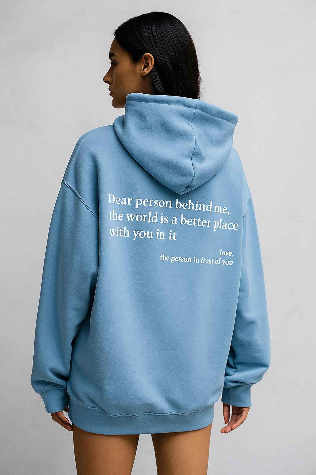 Person wearing a light blue hoodie with a motivational quote on the back against a plain background