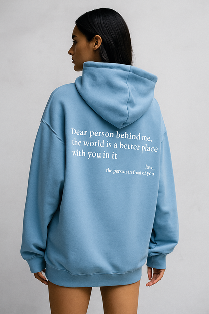 Person wearing a light blue hoodie with a motivational quote on the back against a plain background