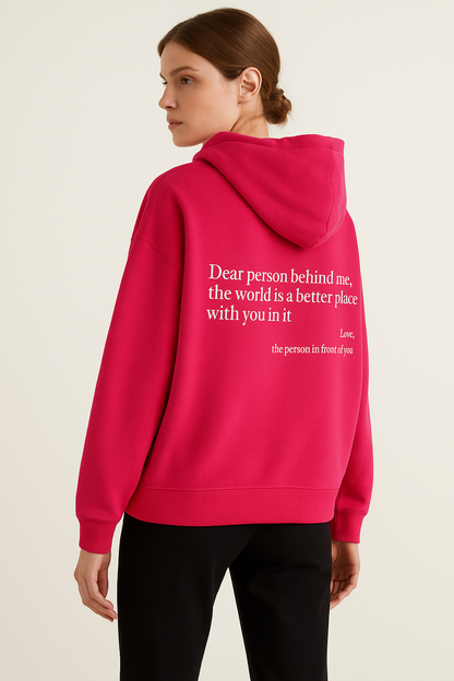 Person wearing a pink hoodie with a message on the back, standing against a plain background