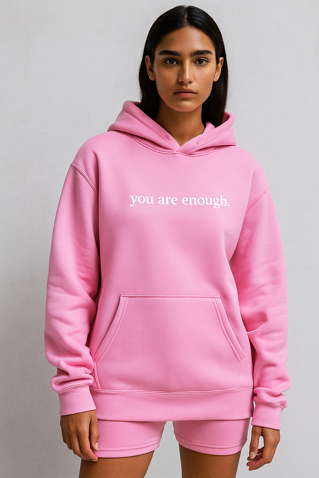 Person wearing a pink hoodie with 'you are enough' text on a plain background