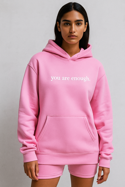 Person wearing a pink hoodie with 'you are enough' text on a plain background