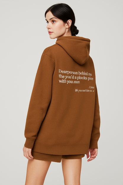 Person wearing a brown hoodie with text on the back against a plain background