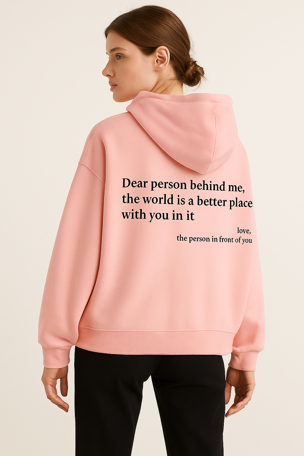 Person wearing a pink hoodie with a message on the back against a beige background